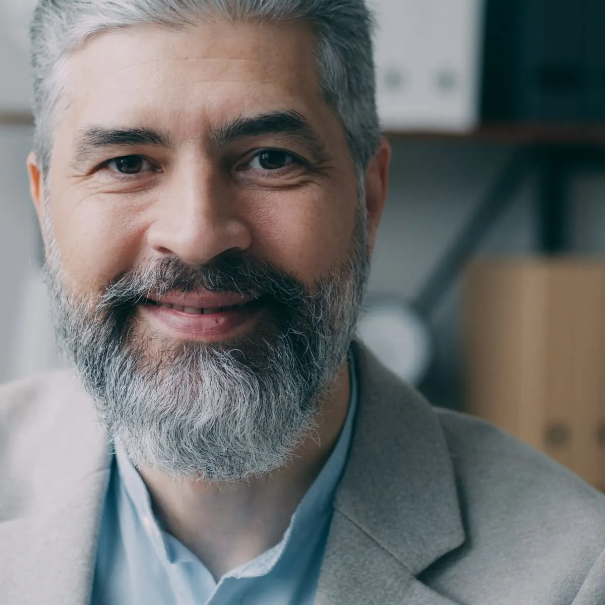 A middle-aged man with a grey beard smiles in a softly lit office.